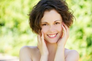 Woman with short brown hair smiling and touching her face