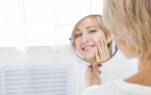 Blonde woman looks at herself in a hand mirror