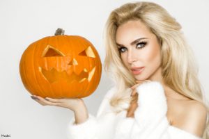 Blonde woman in a fluffy white sweater holding a jack-o'-lantern