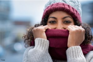Cozy woman in a knit hat and sweater holding a scarf in front of her lower face