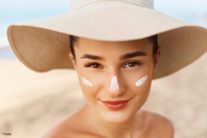 Woman on the beach in a sun hat with sunscreen on her cheeks and nose