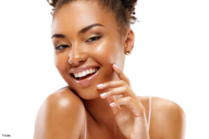 Joyful woman with bright, dewy skin gently touching her face and smiling