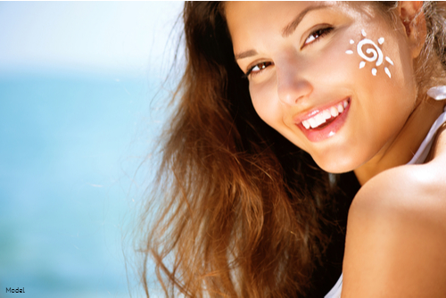 Joyful woman smiling in the sun at the beach with a sun drawn on her cheek in sunscreen