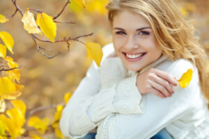 Joyful young blonde woman sitting outdoors in the fall in a white blouse
