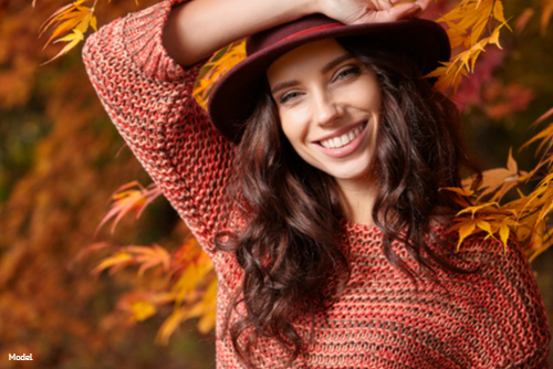 Woman smiling outdoors in the fall wearing a red and orange sweater