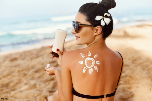 woman smiling on the beach, holding a bottle of sunscreen