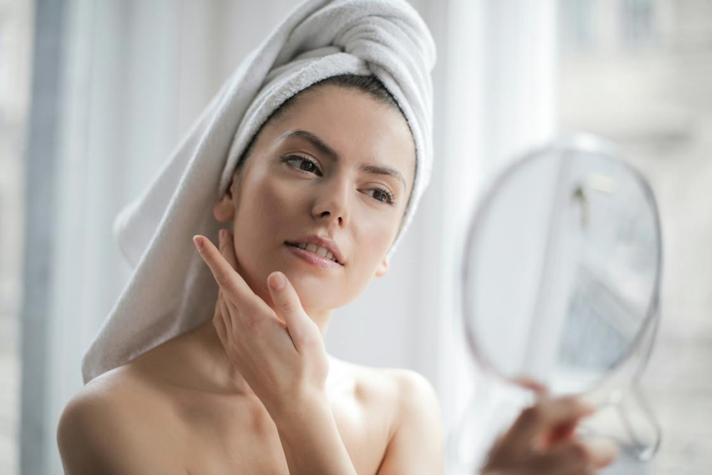 woman with towel on head, performing skincare routine