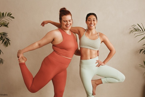 Two confident woman, one thin and one plus-size, in activewear smiling with their arms around each other